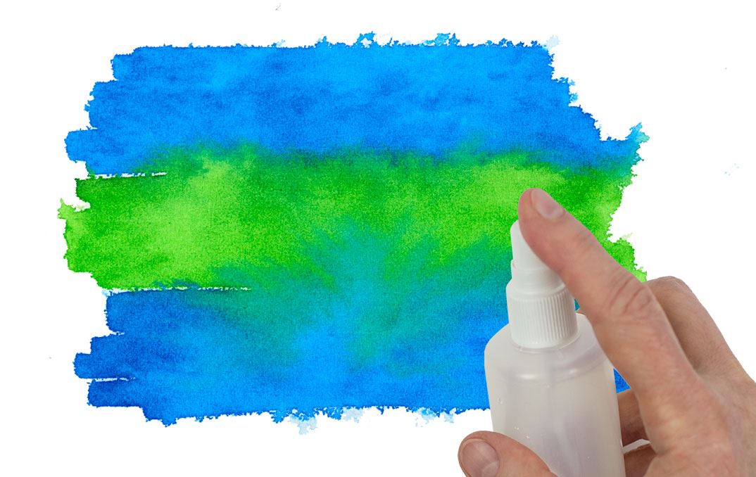 A hand spraying water on a blue and green colour field with a misting bottle.